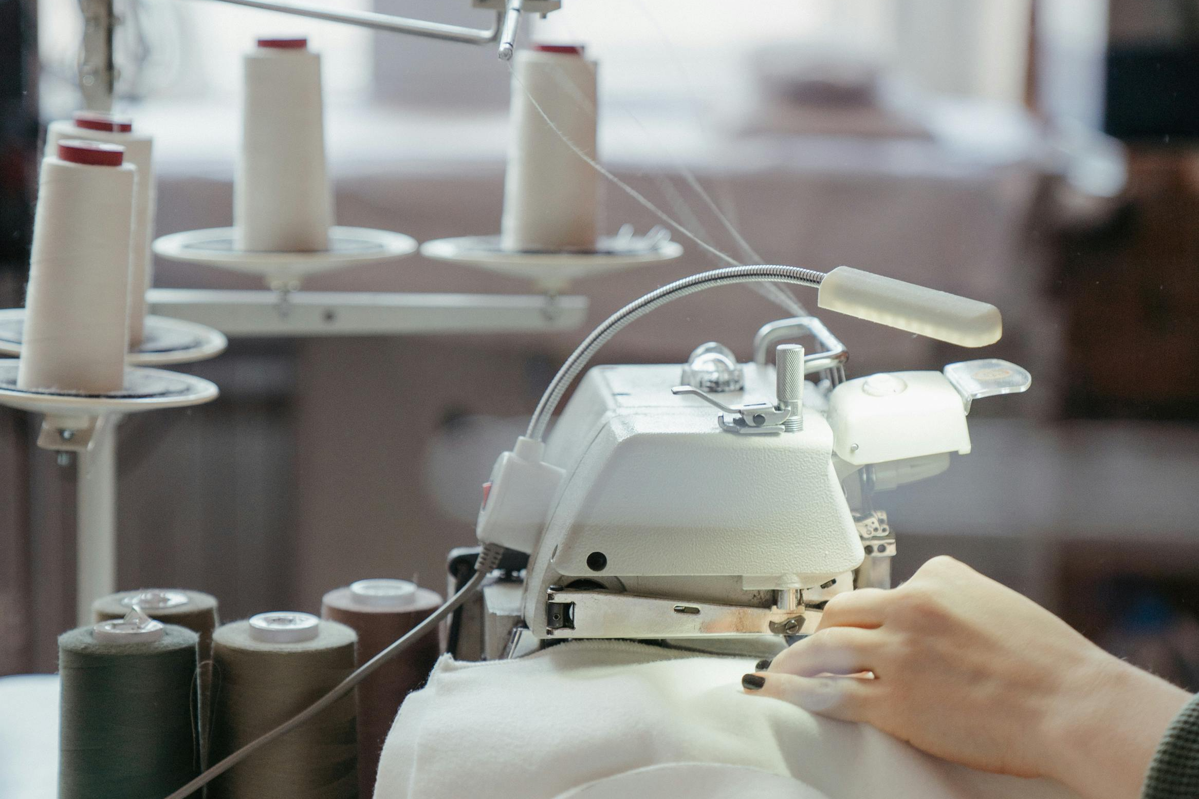 Person operating a sewing machine with spools of thread in the background